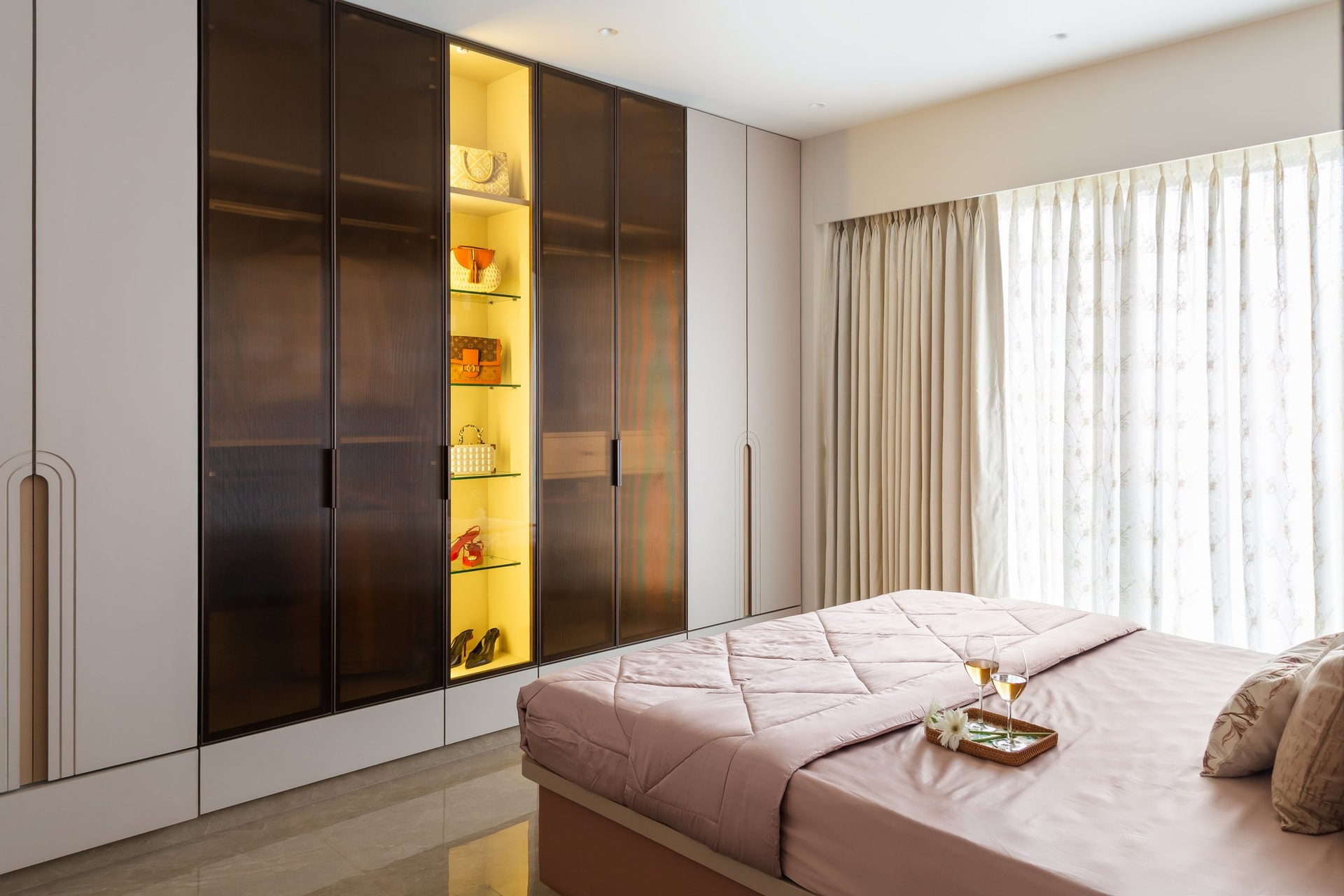 The wardrobe wall, with smoked glass fronts and an amber-lit display column that turns storage into a dressing composition